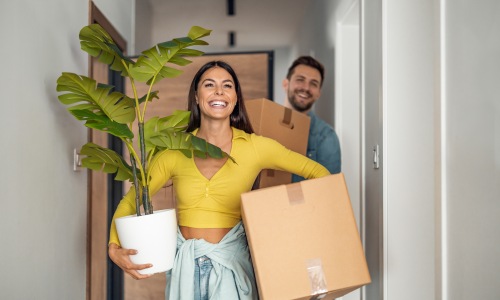 Couple moving into a new apartment with boxes and plants, illustrating the excitement of apartment hunting in Frisco, Texas.