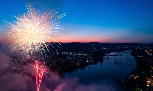 Fourth of July fireworks lighting up the sky at sunset over a river and bridge Fourth of July fireworks lighting up the sky at sunset over a river and bridge