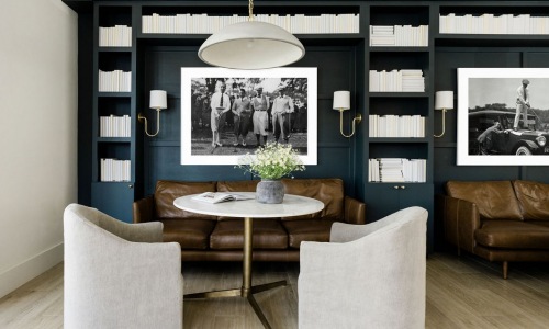 Comfortable lounge area with dark blue bookshelves, brown leather couches, a white marble table, and beige chairs. Framed black-and-white photos of historical scenes on the wall.