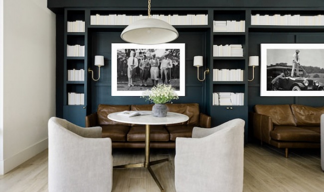 Chic lounge area with leather sofas, a round marble table, and upholstered chairs, set against a dark built-in bookshelf with white books and black-and-white vintage photos, creating a modern yet classic atmosphere. Chic lounge area with leather sofas, a round marble table, and upholstered chairs, set against a dark built-in bookshelf with white books and black-and-white vintage photos, creating a modern yet classic atmosphere.