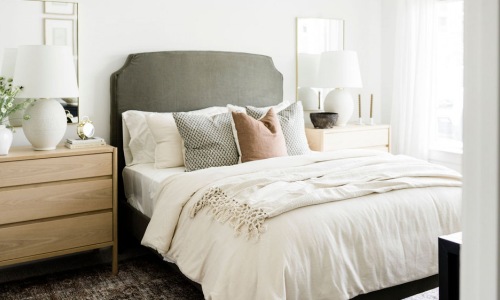 Modern bedroom with a neutral color palette, featuring a cozy bed with layered pillows, wooden nightstands, and soft natural lighting.