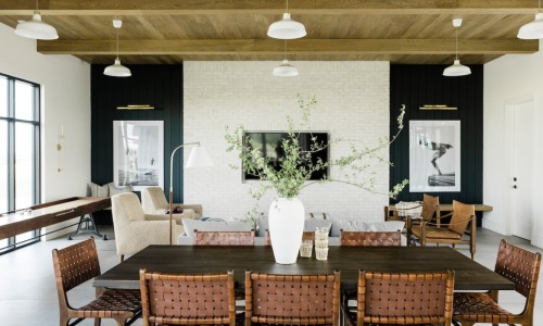 Modern open-concept living and dining room with wood beam ceiling, leather chairs, and shuffleboard table. Modern open-concept living and dining room with wood beam ceiling, leather chairs, and shuffleboard table.